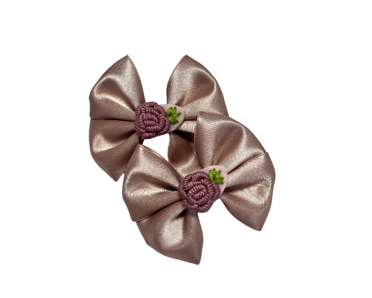 Two metallic gold hair bows with purple flowers on a white background
