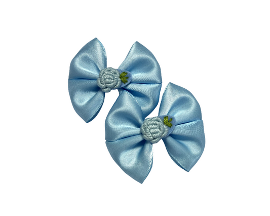 Two light blue satin bows with green centers on a white background