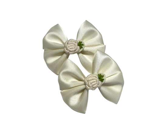Two cream satin hair bows with floral centers on a white background