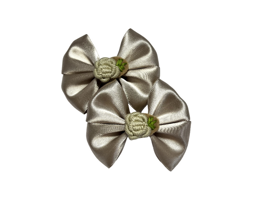 Two silver satin hair bows with green centers on a white background