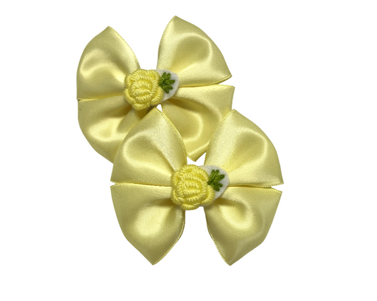 Two yellow satin hair bows with floral centers on a white background