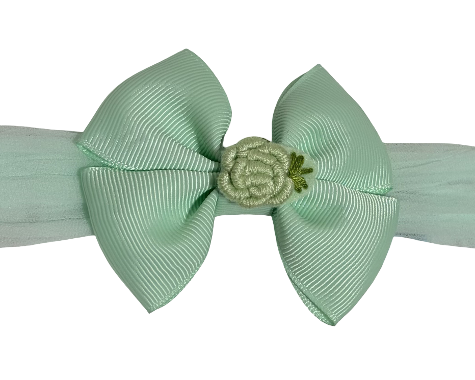 Light green headband with a large bow and small flower detail on a white background