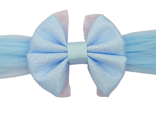 A light blue tulle hair bow with a matching light blue elastic band, featuring a central light blue ribbon and subtle pinkish-blue edges on the bow loops.