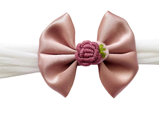 Pink satin bow with a floral center on a white background