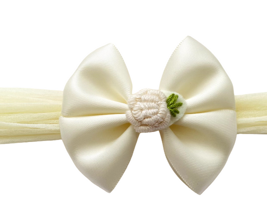 Cream-colored bow hair accessory with a small green flower on a white background