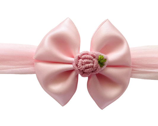 Pink headband with a large bow and floral center on a white background