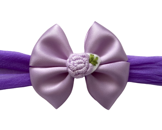 Purple headband with a large bow and small flower on a white background