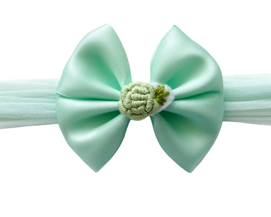 Mint green headband with a bow and flower detail on a white background