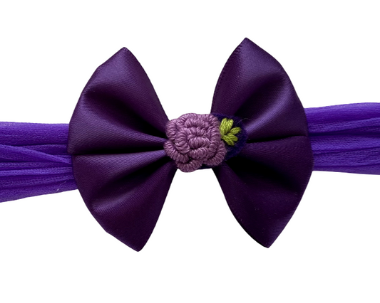 Purple headband with a large bow and floral center on a white background
