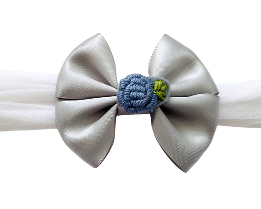 White headband with a large silver bow and a small blue flower in the center on a white background