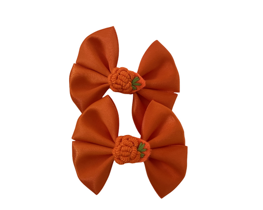 Pair of orange hair bows with pumpkin designs on a white background